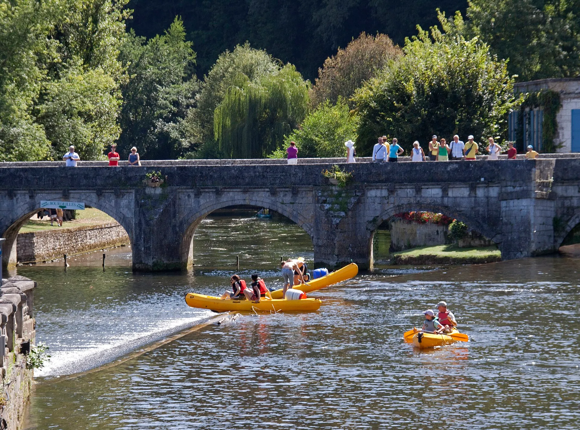 Des canoës et des kayaks jaunes franchissent le barrage sous le pont, dans la traversée de Brantôme