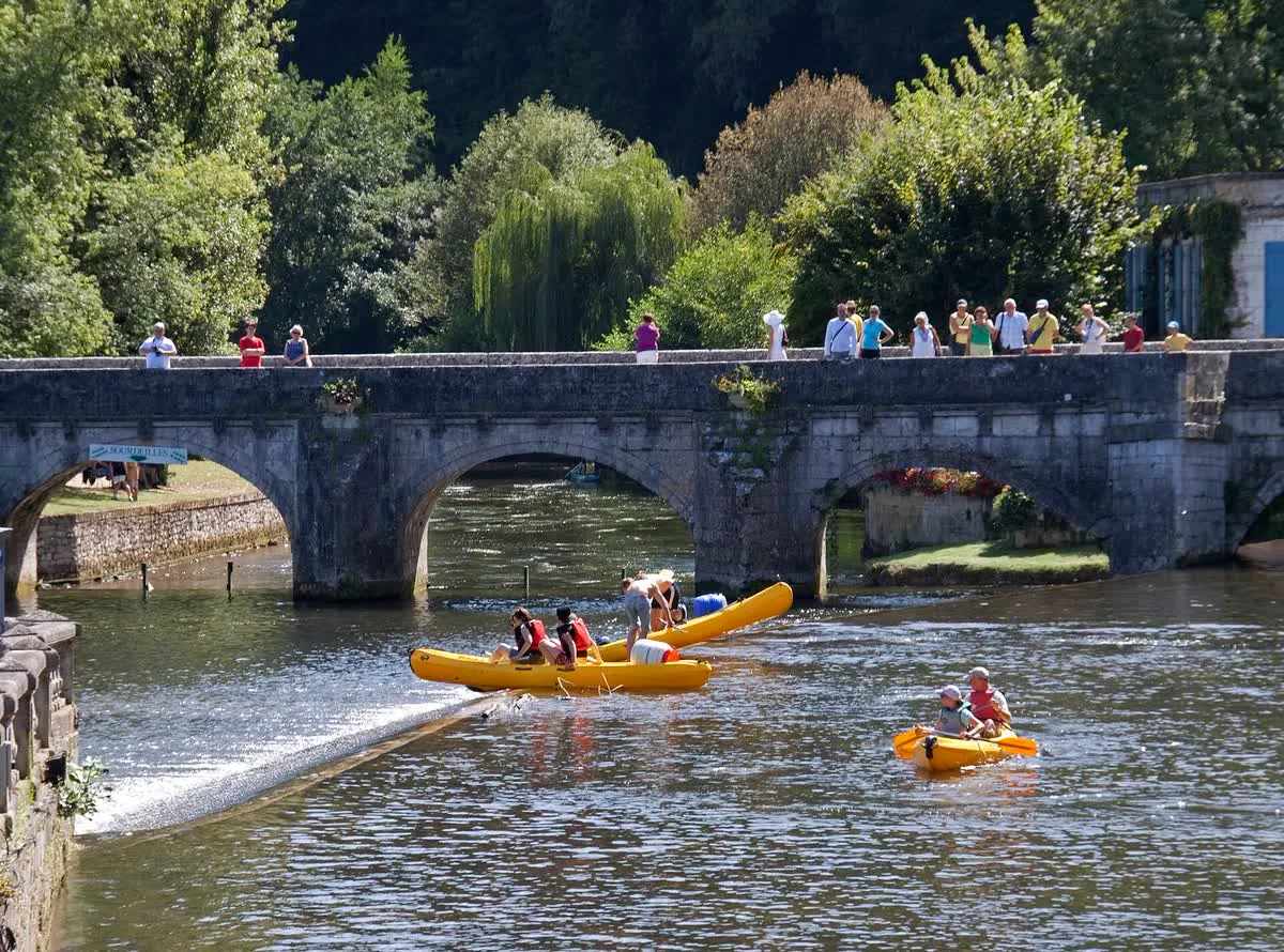 Des canoës et des kayaks jaunes franchissent le barrage sous le pont, dans la traversée de Brantôme